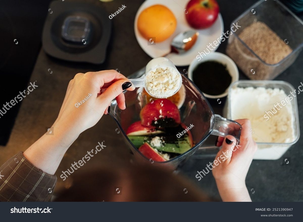 Adding a scoop of plant protein powder into a blender of fresh fruit and greens