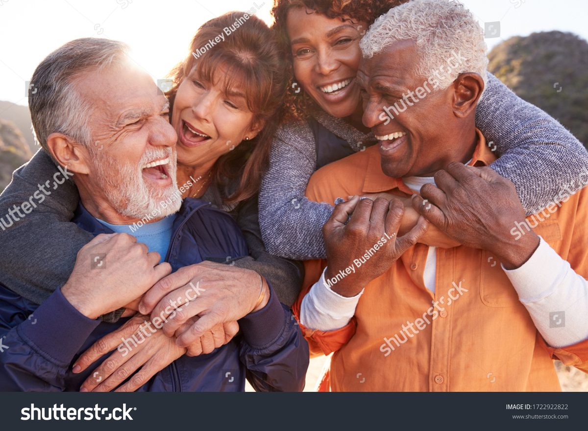 A group of older friends laughing and embracing outdoors in the sunshine