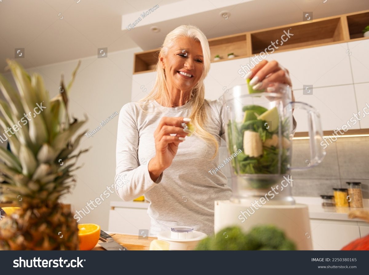 A smiling older woman making a fresh green smoothie in her kitchen